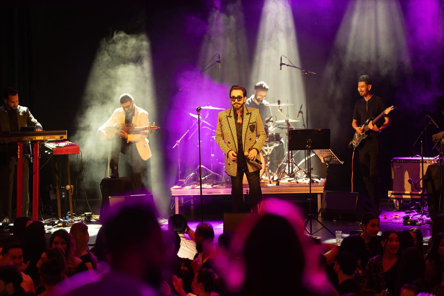 Habib Qaderi performing live on stage with his band, bathed in purple and blue light